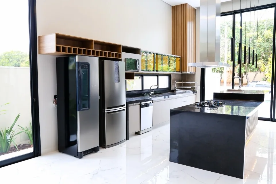 Cozinha gourmet planejada com ilha em granito preto, cooktop e nicho de madeira para adega