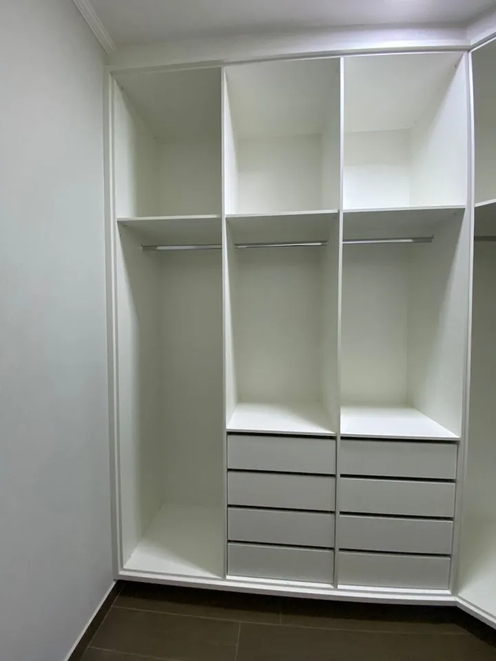 Detalhe de closet planejado em MDF branco com gaveteiros duplos, prateleiras e cabideiro ao fundo