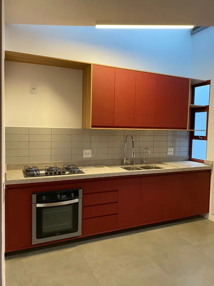 Cozinha compacta em linha com armários em MDF terracota, moldura em madeira natural, bancada de granito bege e forno embutido