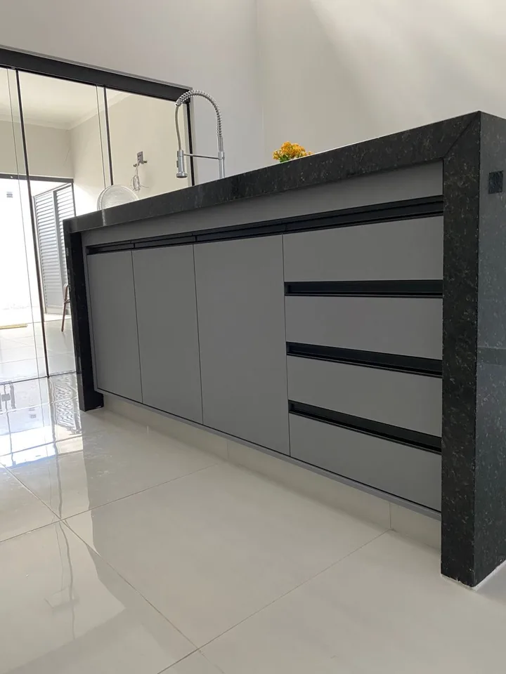 Detalhe de ilha de cozinha em MDF cinza com puxadores pretos embutidos e tampo espesso de granito preto