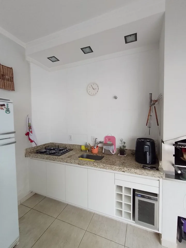 Cozinha compacta em MDF branco com bancada de granito bege, adega elétrica embutida e nichos para garrafas