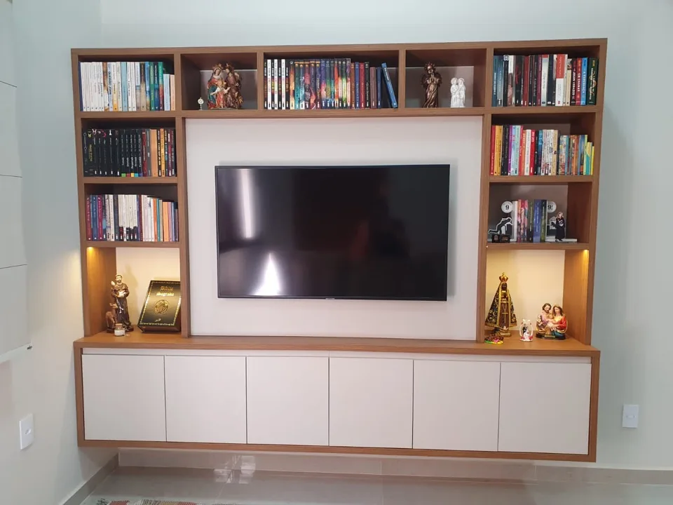 Estante planejada em madeira com nichos para livros, painel de TV e iluminação embutida