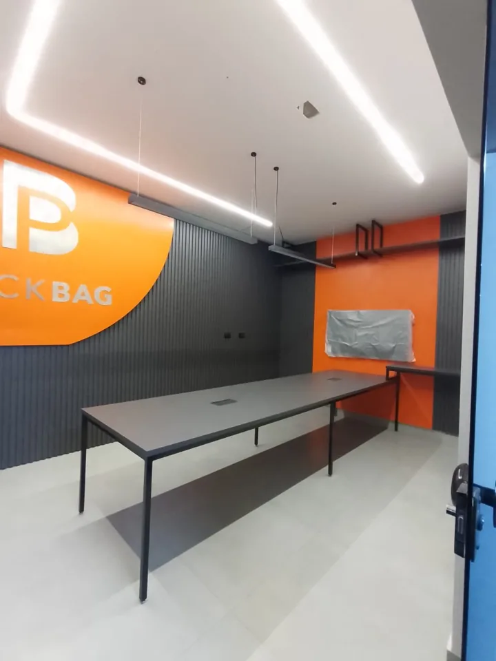 Sala de reunião planejada com mesa longa cinza-grafite e parede laranja com logotipo do cliente