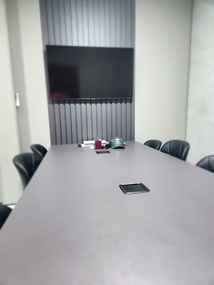Sala de reunião planejada com mesa grafite, painel ripado preto e TV embutida
