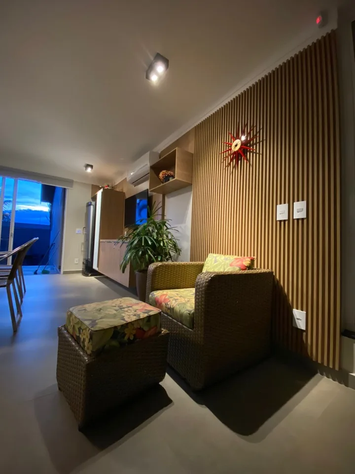 Sala de estar com parede ripada em madeira, relógio decorativo e vista para varanda com piscina ao fundo